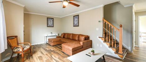 A living room with a sectional sofa, a white coffee table, a wooden floor, a ceiling fan, and a staircase.