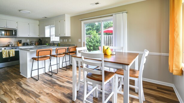 Una cocina moderna con armarios blancos, una isla de madera y un comedor con sillas blancas y una mesa de madera.