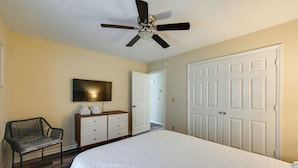 A bedroom with a bed, a ceiling fan, a TV, a chair, a dresser, and a door. - Easy ECU Access: Modern Home w/ Patio! (Greenville)