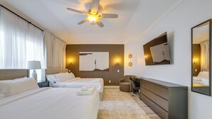 Quarto de hotel com duas camas, uma escrivaninha, uma cadeira, ventoinha no teto e um espelho grande.
