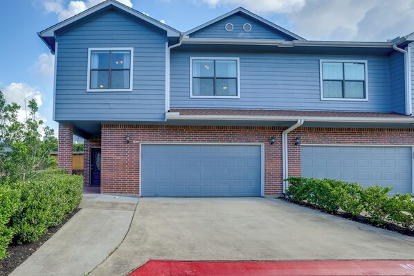 A two-story house with a blue exterior, two garage doors, and a brick foundation.