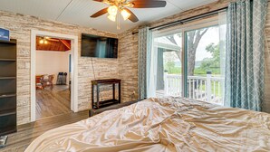 Un dormitorio con una cama grande, ventilador de techo, chimenea y vistas al exterior.