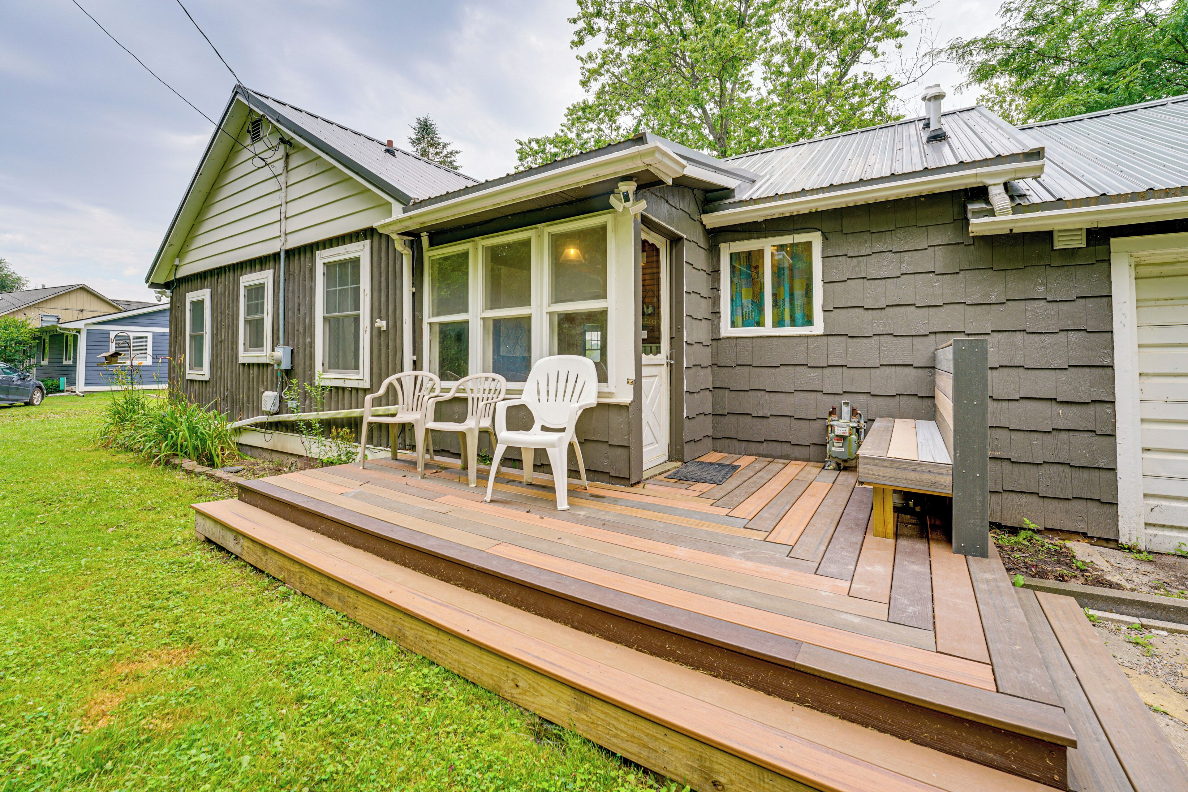 A house with a wooden deck, white chairs, and a small table.