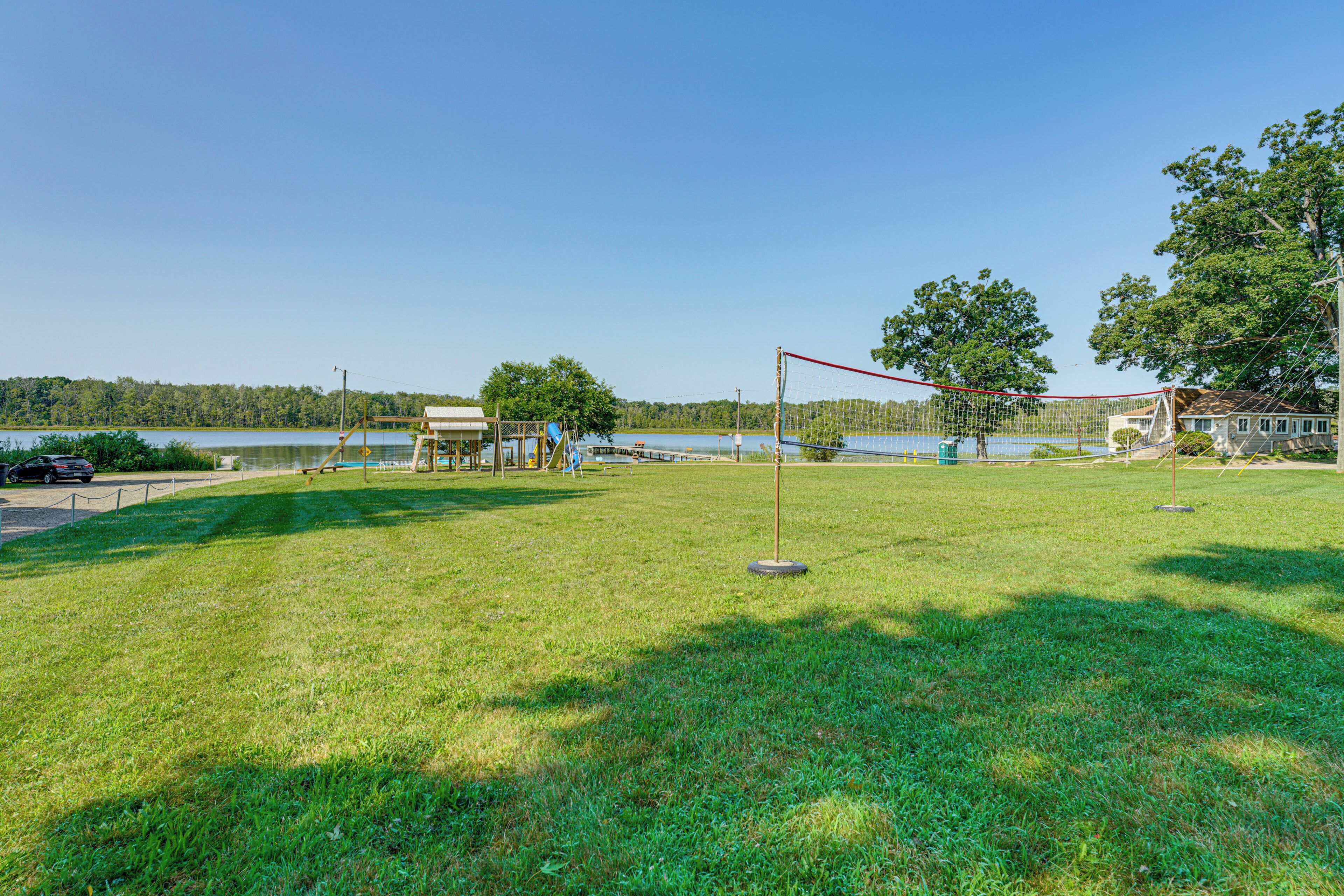 Ein Rasenplatz mit einem Netzvolleyballfeld, ein kleines Gebäude und ein See im Hintergrund.