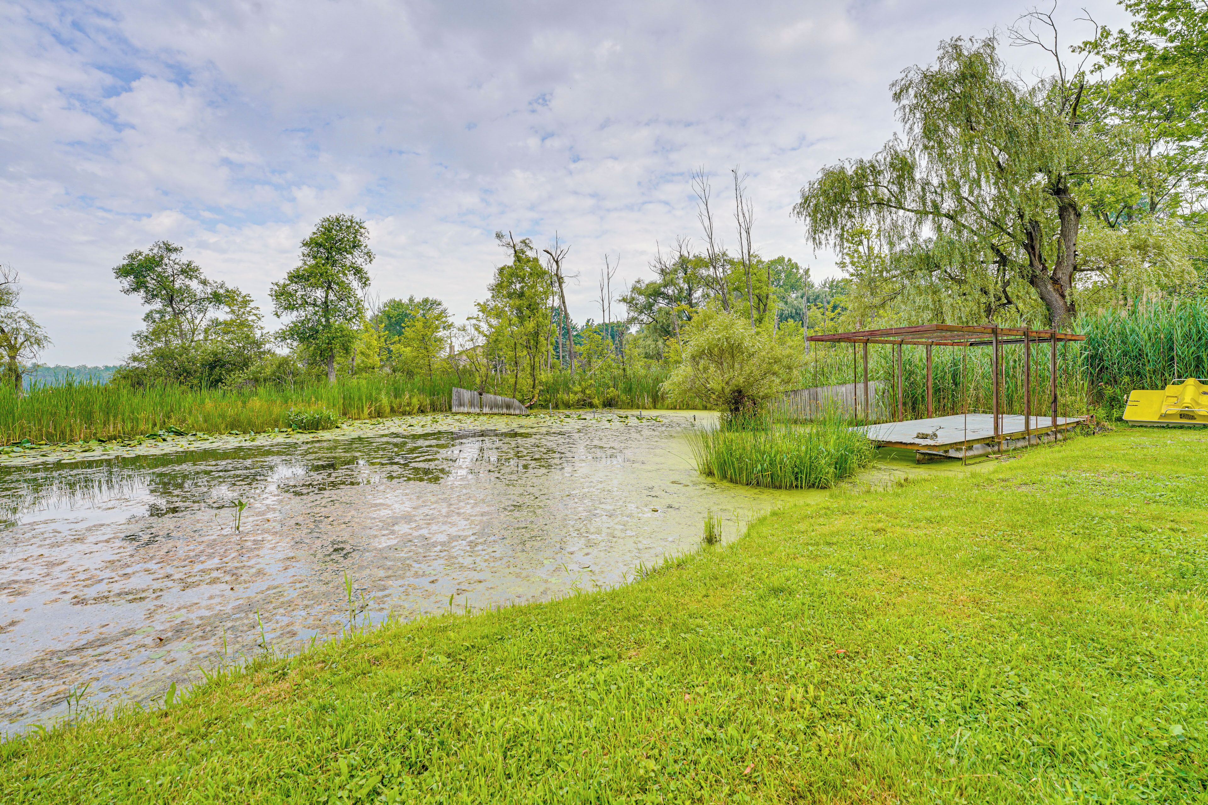 A pond with a wooden deck and a gazebo in a grassy area with trees.