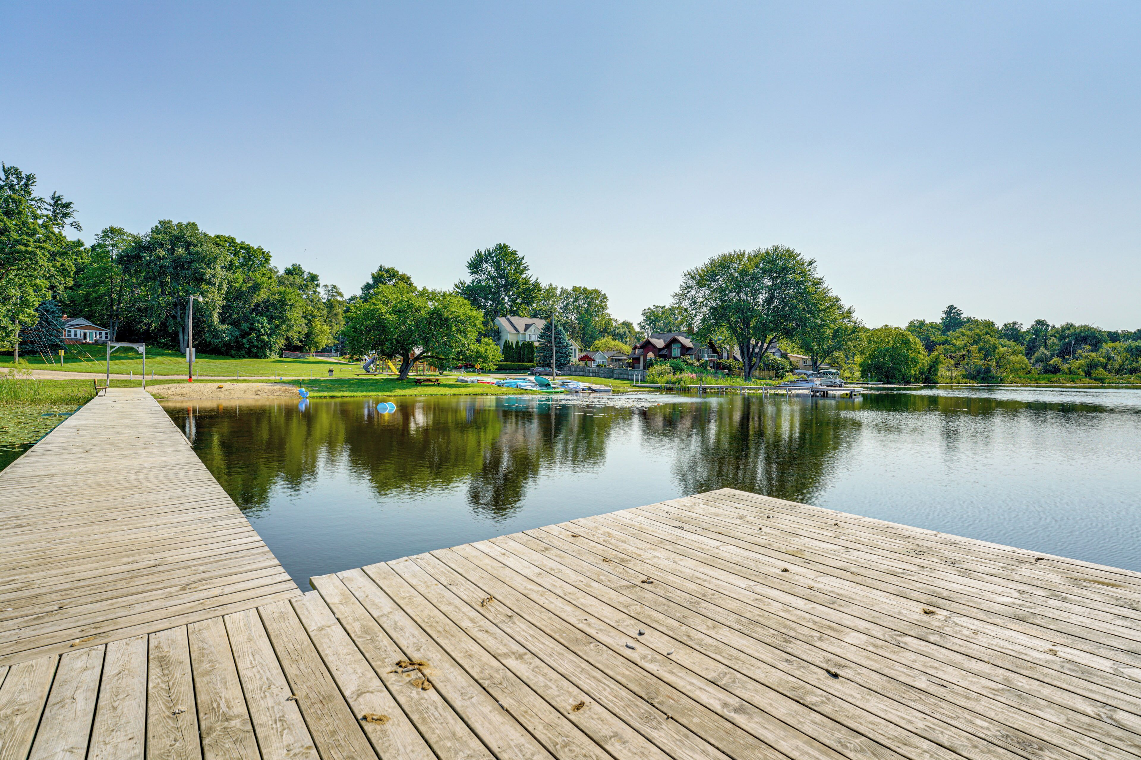 A wooden dock extending into a calm lake with houses and trees in the background.