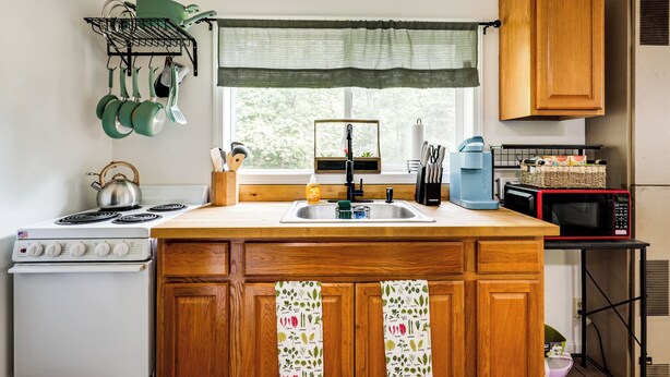 A kitchen with wooden cabinets, a stove, a sink, and a window with a view of trees. - Private UP Escape Near Lake Superior (Pelkie)