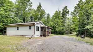 A single-story cabin with a porch, surrounded by a gravel driveway and a forested area. - Private UP Escape Near Lake Superior (Pelkie)