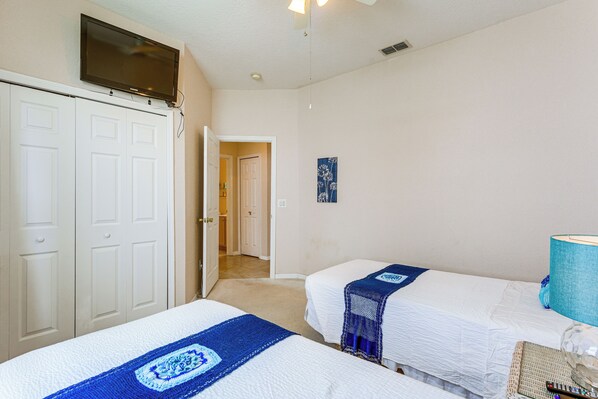 A hotel room with two beds, a TV mounted above the door, and a hallway leading to another room.