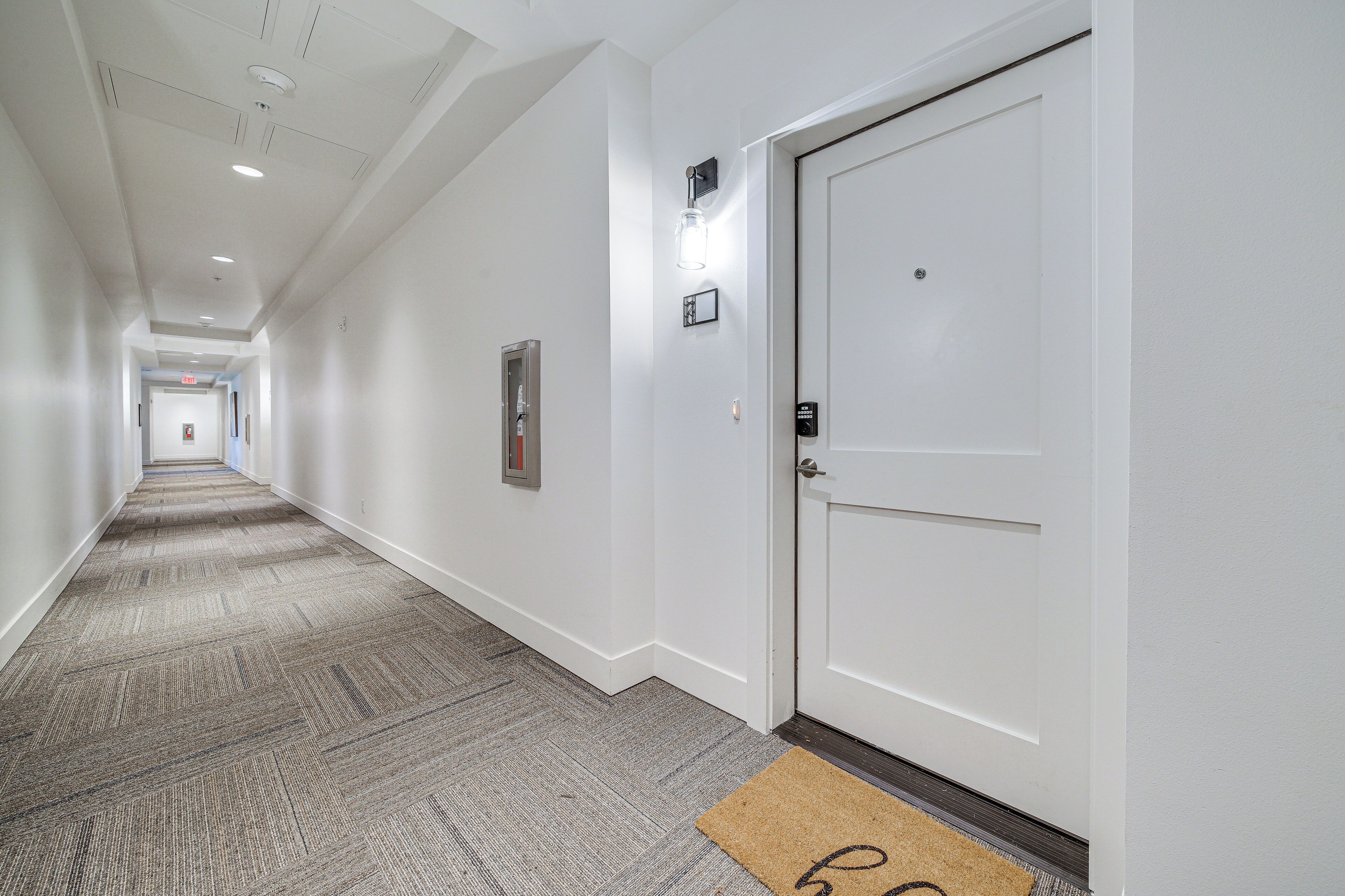 A hallway with a carpeted floor, white walls, and a door with a doormat.