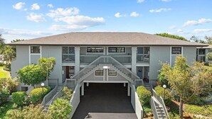 A two-story building with a central staircase, a covered entrance, and a parking area.