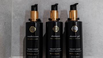 Trois flacons noirs ornés de détails dorés, étiquetés « après-shampoing », « shampoing » et « gel douche », chacun étant doté d’un bouchon doré et d’un logo circulaire.