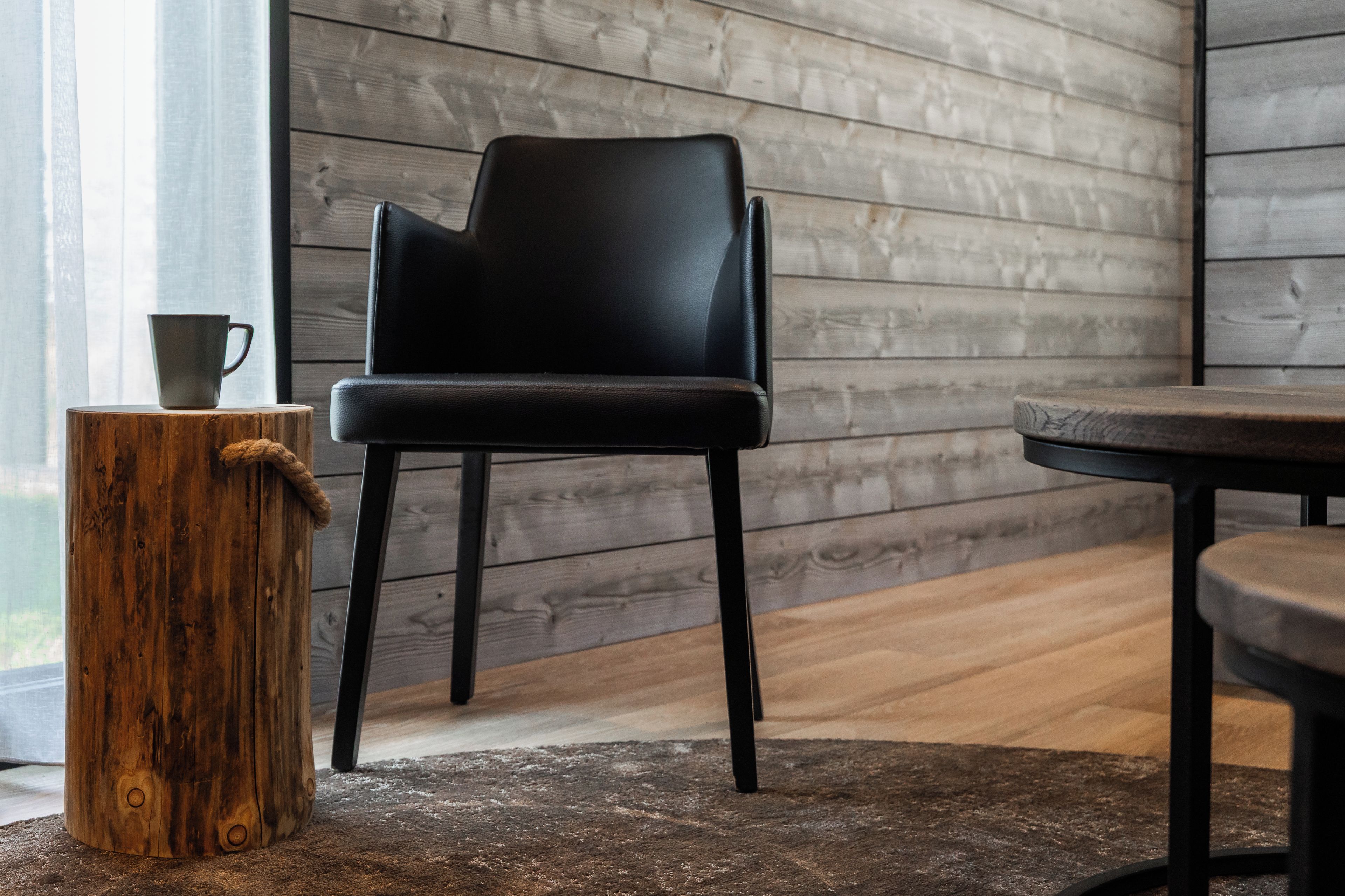 Un interno moderno con una poltrona in pelle nera, uno sgabello di legno con una tazza e un tavolo.