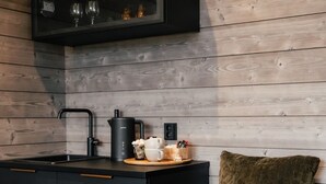 A modern kitchen with black cabinetry, a wooden wall, a built-in wine rack, and a small seating area with a cushion. - Lapland Winter Park  (Rovaniemi)