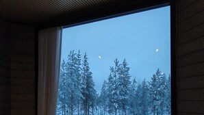 Ein Schlafzimmer mit einem großen Fenster und Blick auf einen verschneiten Wald.