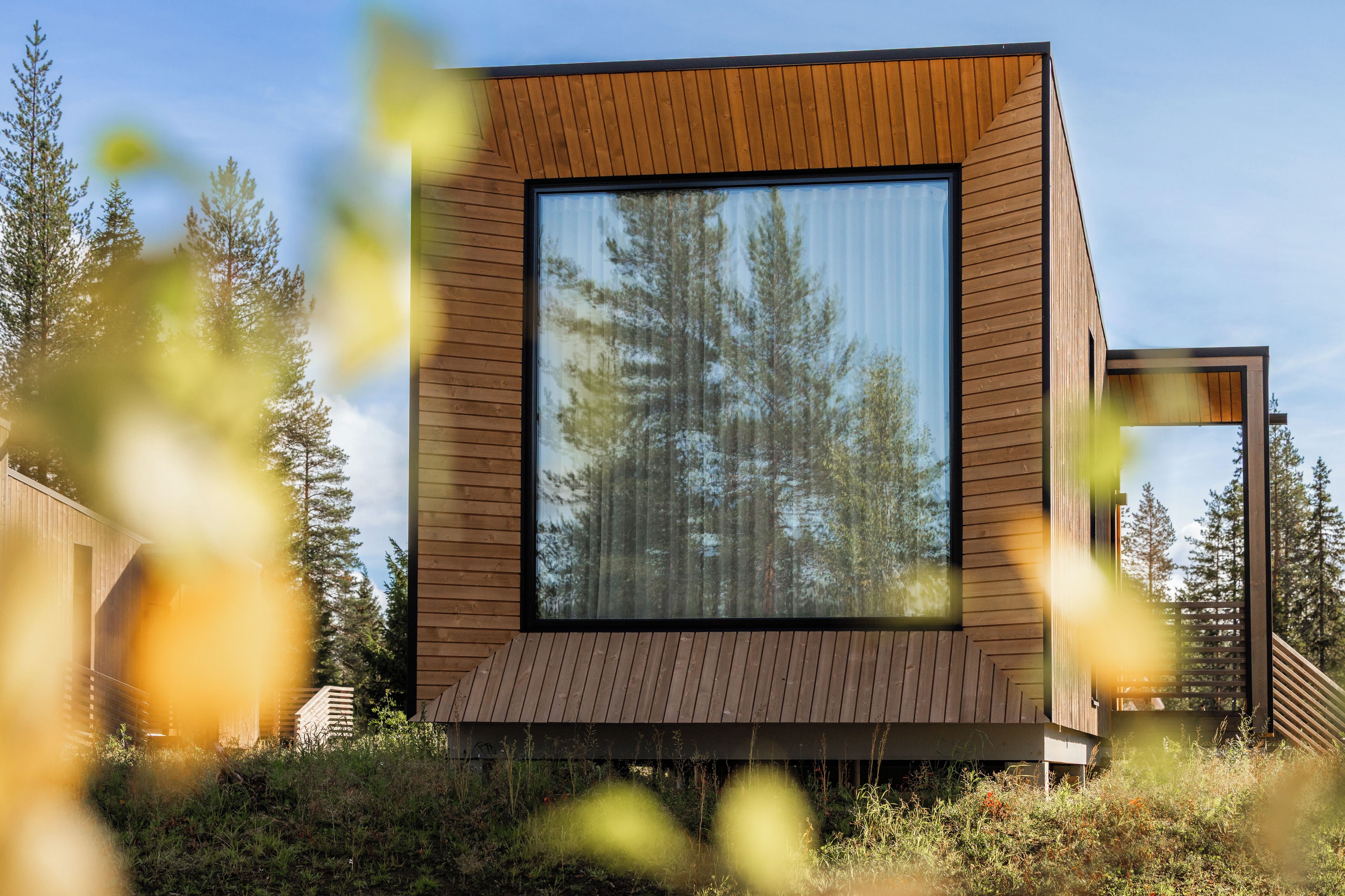 Una cabaña de madera moderna con un ventanal grande, rodeada de árboles.