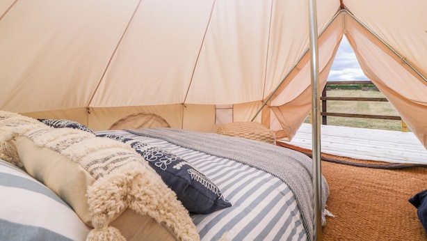 Tenda com cama interna, com um cobertor listrado e almofadas.