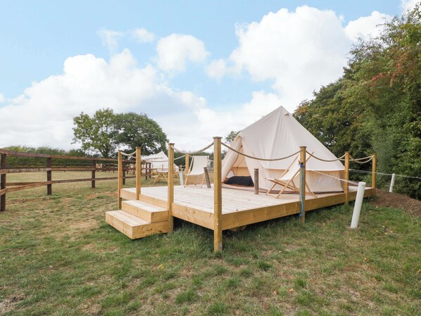Une grande tente blanche en forme de pyramide, dotée d’une terrasse en bois à l’avant, entourée d’une barrière en corde et d’une clôture en bois.