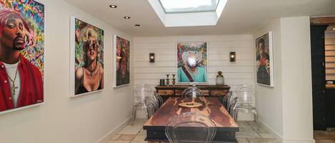 A dining area with a long table, clear chairs, and a skylight above.