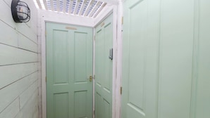 Un estrecho pasillo con puertas verde claro, suelo de madera y techo blanco con tragaluz.