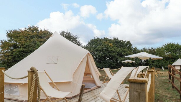 Un espacio con carpas, una terraza de madera, una barrera de cuerda y una silla de descanso.