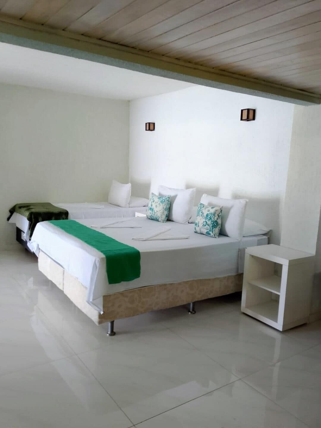A hotel room with a large bed, a bedside table, and a small shelf.