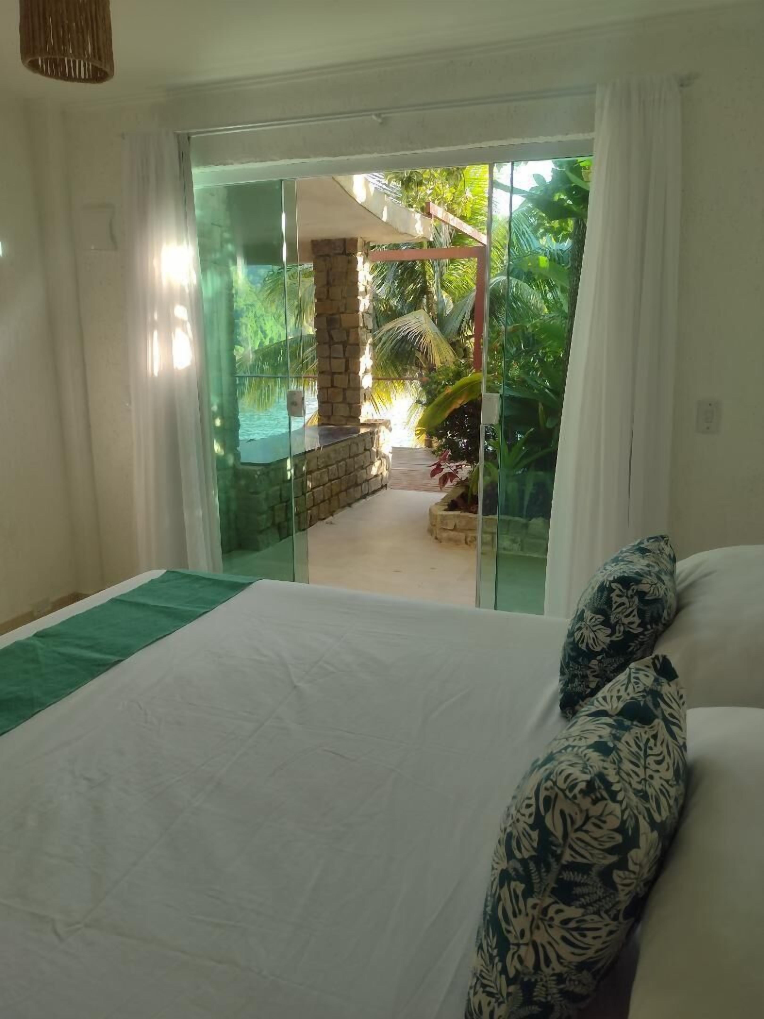A bedroom with a large bed, a view of a garden through a glass door, and a stone pillar.