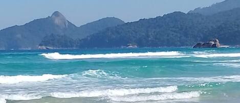 Una playa con aguas turquesas cristalinas, olas suaves y un telón de fondo montañoso.