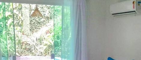Un dormitorio con cama, lámpara colgante, puerta corrediza de vidrio que da a un balcón y un equipo de aire acondicionado en la pared.