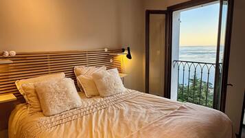 Une chambre avec un grand lit, une table de chevet, une lampe et une vue sur la mer depuis un balcon.