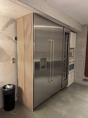 A stainless steel refrigerator with a wooden panel design, a built-in oven, and a trash bin.