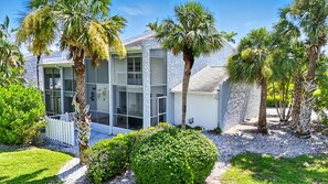 A modern house with large windows, surrounded by palm trees and a well-maintained garden.