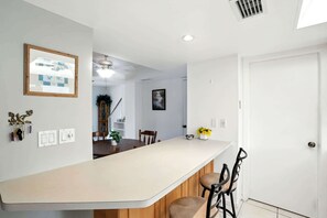A modern kitchen with a central island, white walls, and a door leading to another room. - Naples Retreat - Walk to Pool and More (Naples)