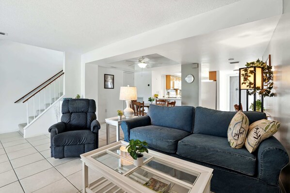A modern living room with a blue sofa, a black armchair, and a glass coffee table.