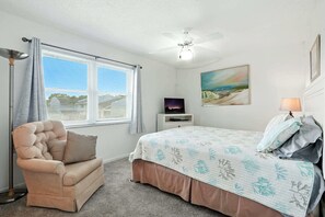 A bedroom with a bed, a sofa, a ceiling fan, a TV on a stand, and a painting on the wall.
