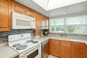 A modern kitchen with wooden cabinets, a white stove, and a large window with blinds.