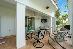 Un patio couvert avec un ventilateur de plafond, un téléviseur fixé au mur, une table à manger avec des chaises et un espace barbecue.