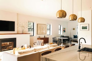 A modern kitchen with a marble island, a dining area with chairs, and pendant lights.