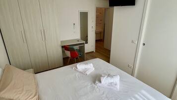 A hotel room with a bed, a desk, a chair, a TV mounted on the wall, and a wardrobe.