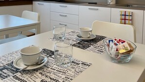 Une cuisine moderne avec un plan de travail blanc, des appareils en acier inoxydable et une fenêtre équipée de stores.