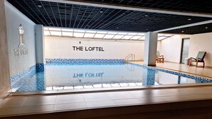 Een binnenzwembad met betegelde vloer en wanden, een plafond met rasterpatroon, en een bordje met de tekst 'THE LOFTEL'.