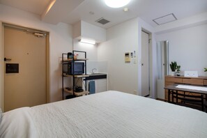 Quarto de hotel com cama, escrivaninha com computador, espelho e uma pequena cozinha.