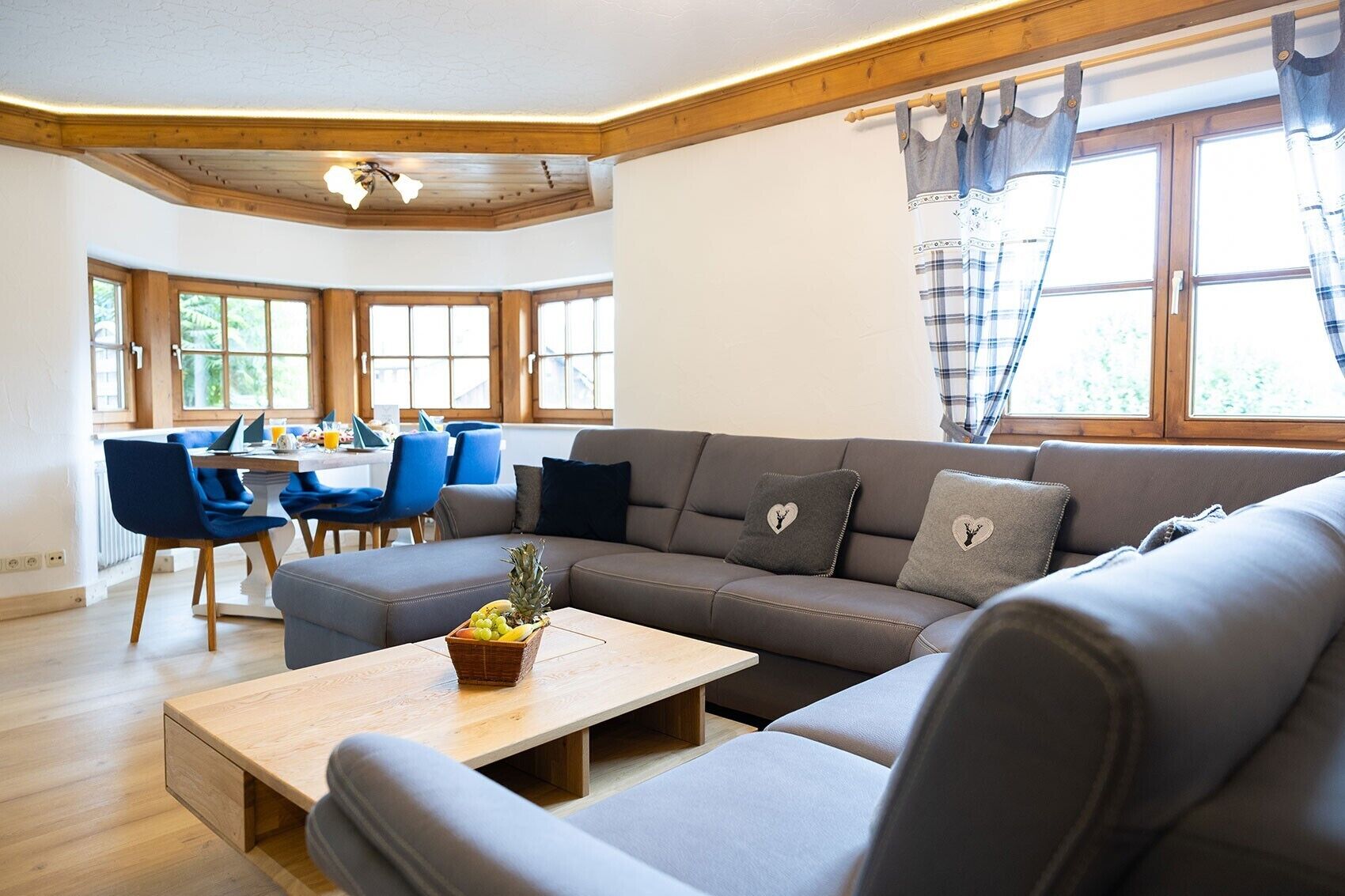 A modern living room with a grey sofa, blue chairs, a wooden coffee table, and a dining area with a table and chairs.