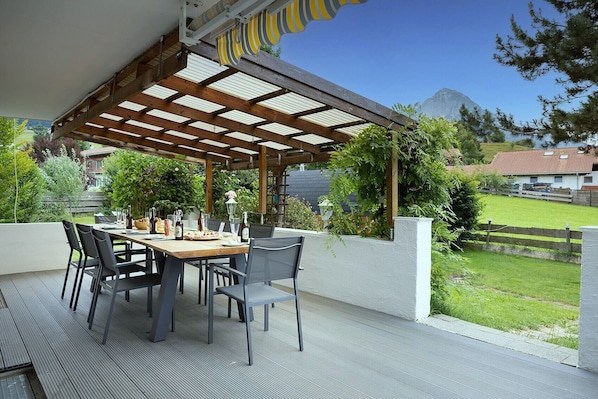 An outdoor patio with a wooden pergola, a table set for dining, and chairs.