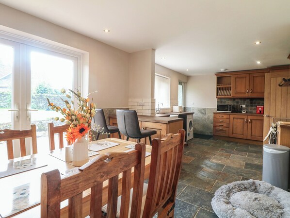 A spacious kitchen with a dining area, large windows, and a stone floor.