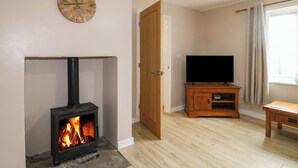 Una sala de estar con una estufa de leña, un televisor sobre un mueble de madera y una puerta que da a otra habitación.