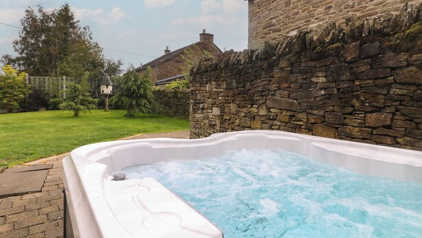 Jacuzzi en un patio trasero con pared de piedra y césped.