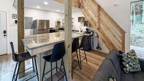 A modern kitchen with a central island, wooden staircase, and a view of the outdoors. - Coal Ridge Cabin - WV Retreat with Family History (Summersville)