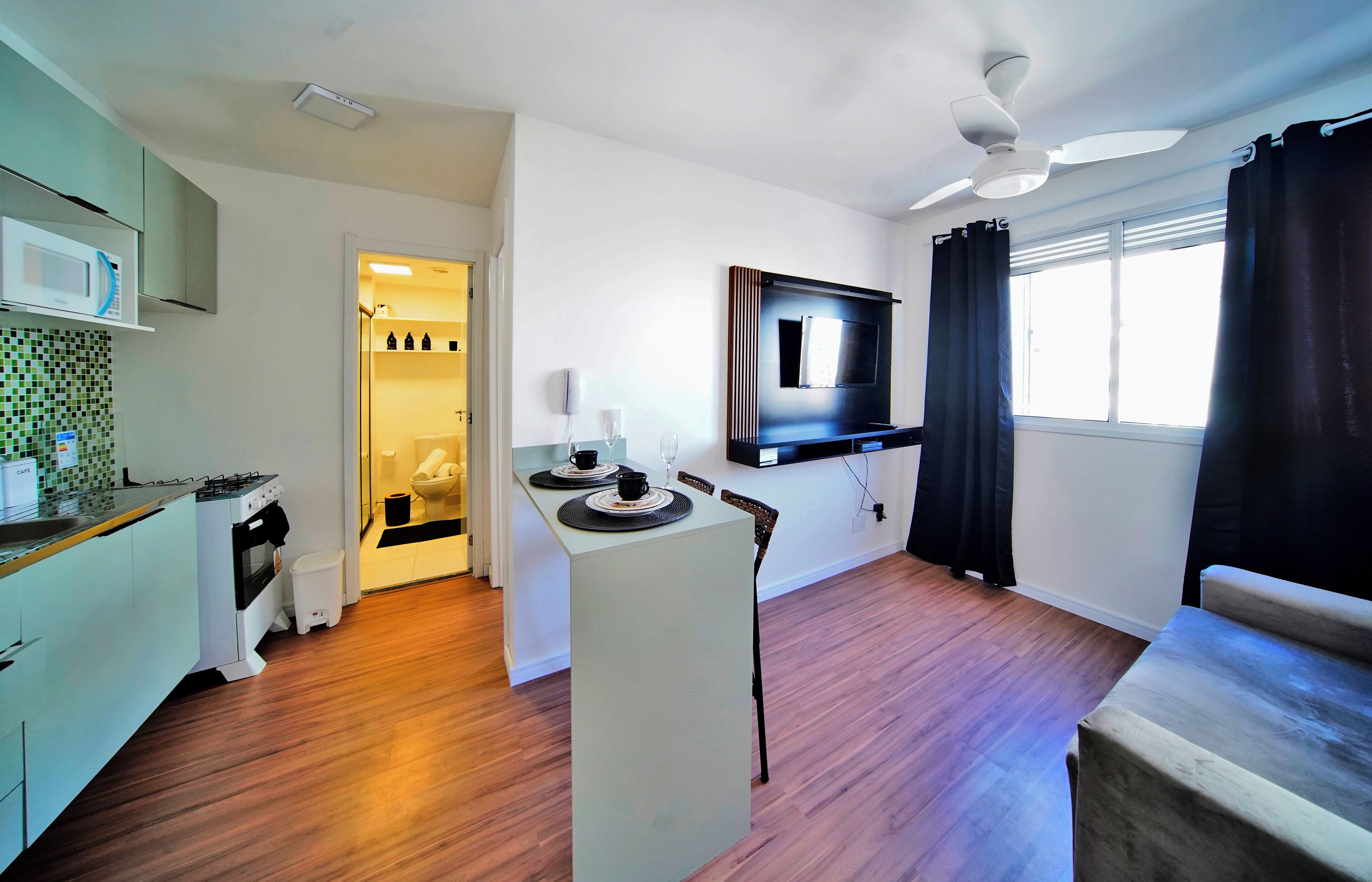 A compact kitchen with a microwave, stove, and sink. There is a dining area with a table and chairs, and a TV mounted on the wall.