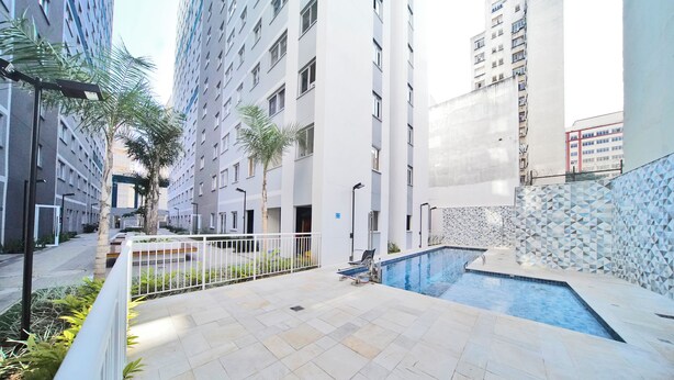 A modern residential building with a swimming pool, a covered patio area, and a view of adjacent high-rise buildings. - Apartamento no centro de SP - 1209A (São Paulo)